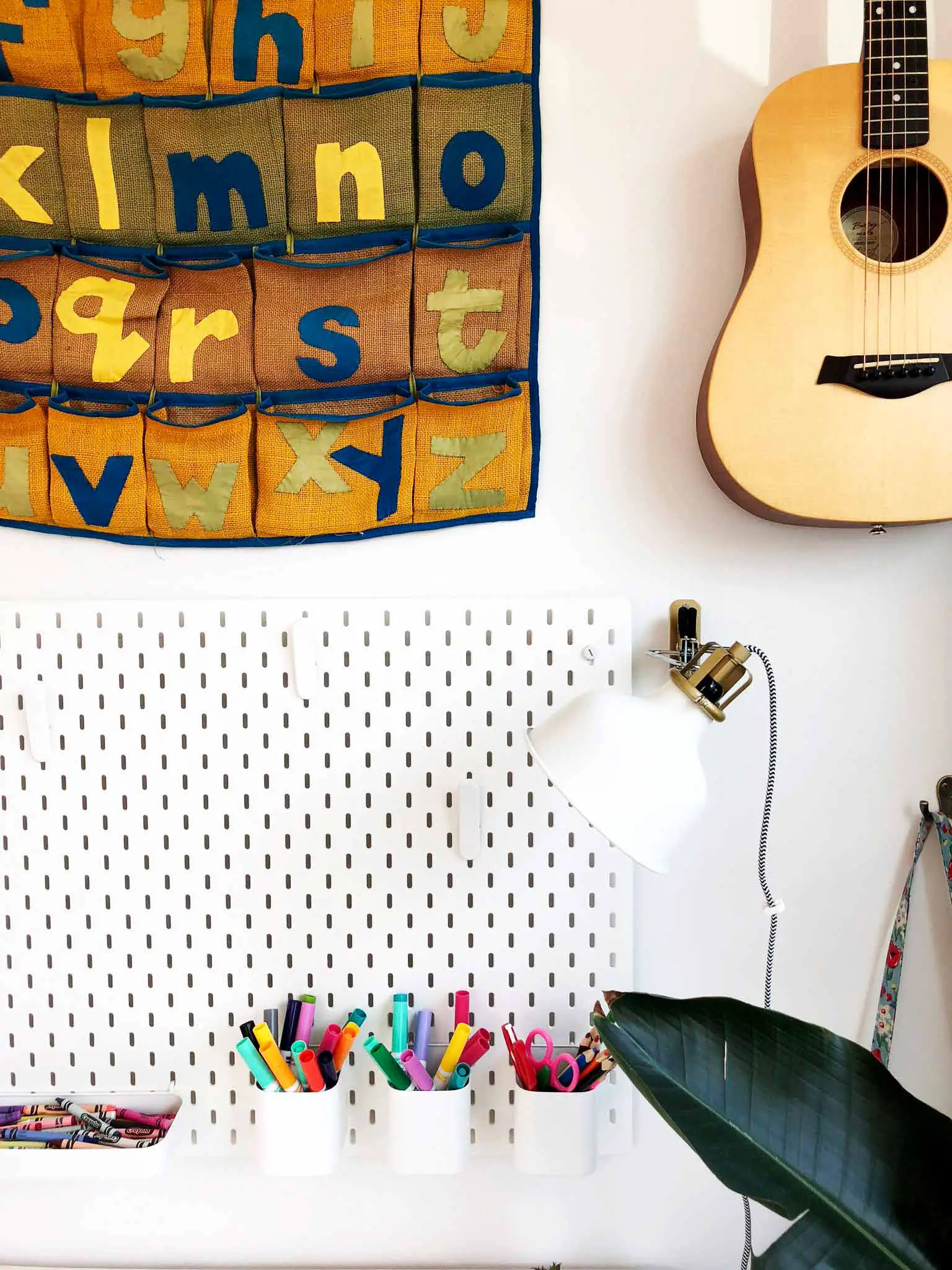 IKEA SKADIS pegboard with pens and crayons, guitar mounted on the wall