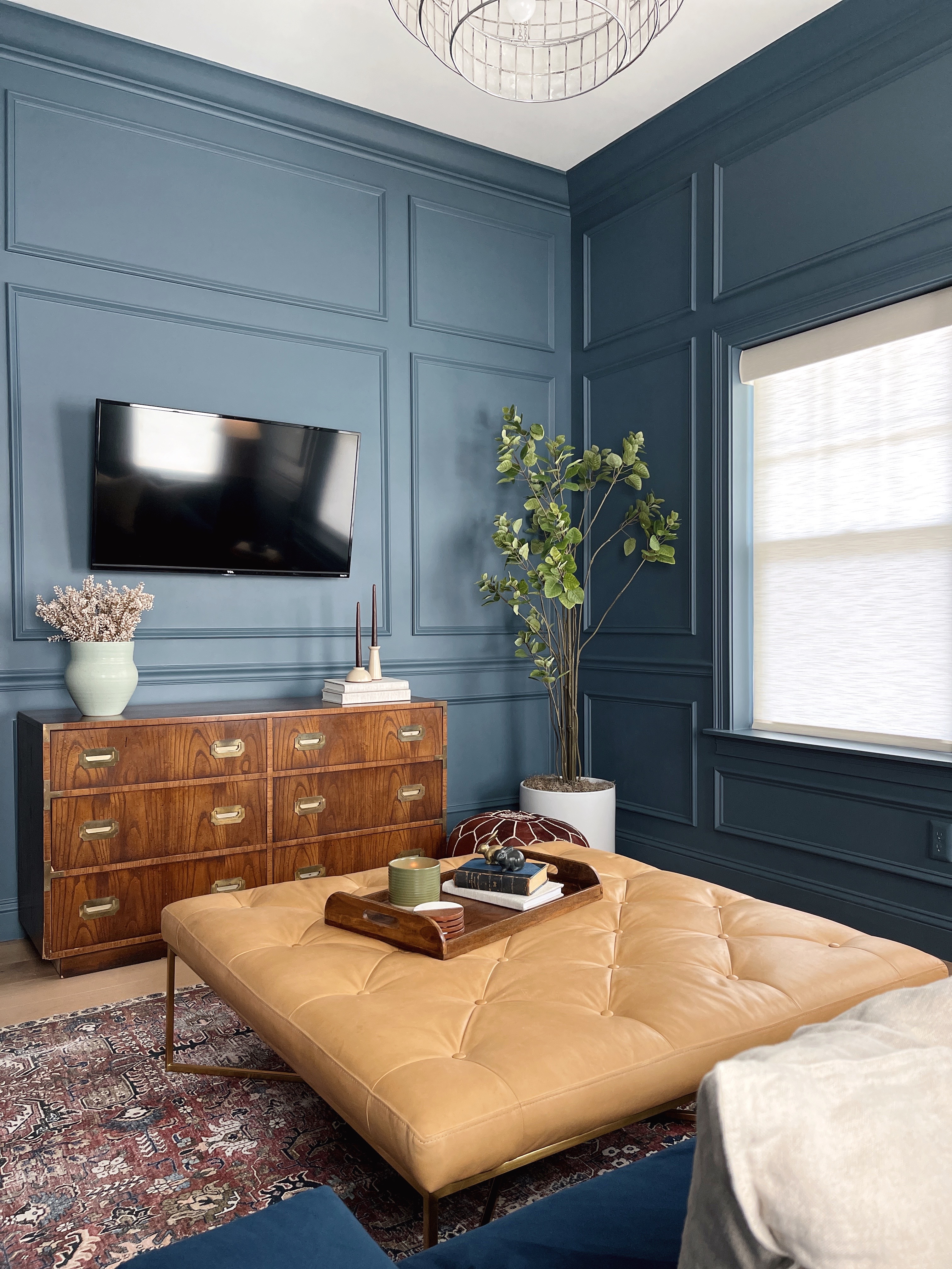 living room with blue picture molding, leather ottoman and blue velvet sofa